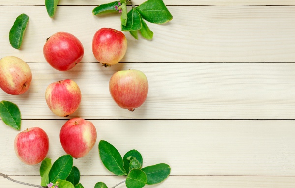 Красные яблоки с зелеными листьями на деревянном столе 