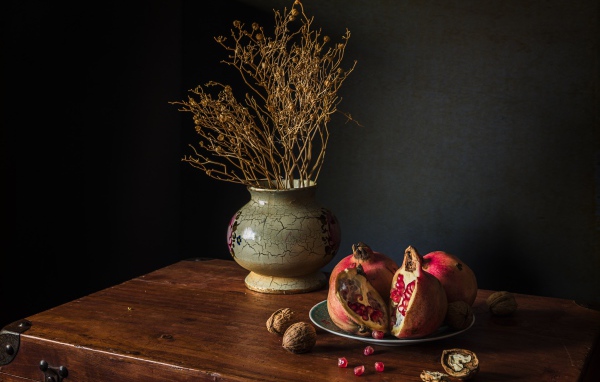 Красный гранат на столе с грецкими орехами и сухой веткой в вазе