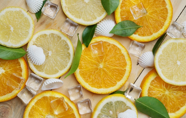 Кусочки апельсина и лимона на столе с кубиками льда и ракушками