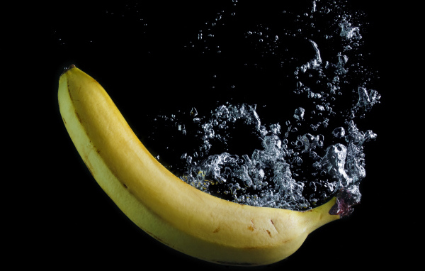 Желтый банан в воде на черном фоне