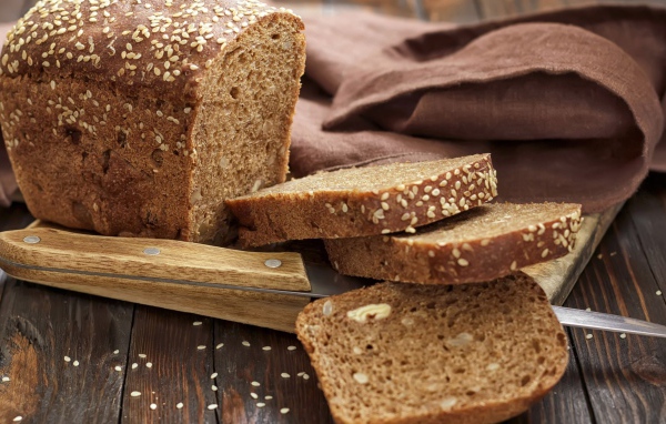 Буханка хлеба нарезанная кусочками на столе с ножом