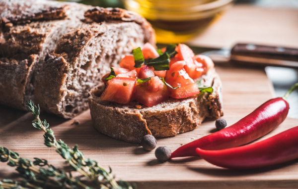 Черный хлеб с кусочками помидора на столе с острым красным перцем