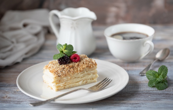 Кусок торта лежит на белой тарелке на столе с кофе