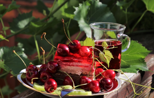 Кусок торта с черешней на столе с чашкой чая 