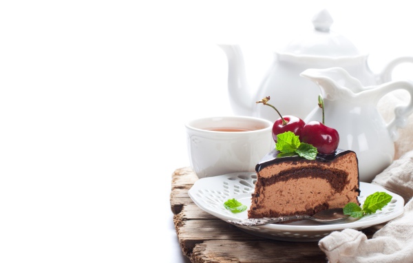 A piece of cake with cherry berries on a table with tea