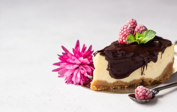 Кусок чизкейка с шоколадом на столе с малиной и цветком