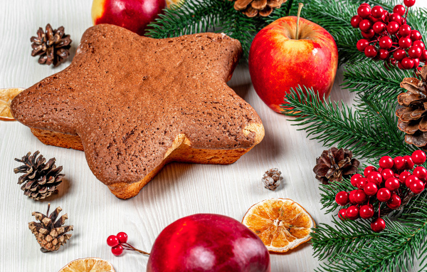 Рождественский кекс на столе с еловыми ветками,  яблоками и шишками