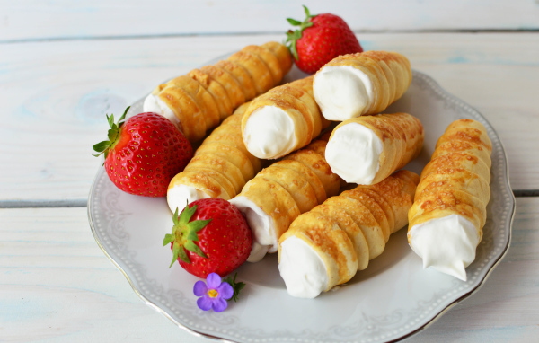 Пирожные трубочки с кремом и ягодами клубники на тарелке 