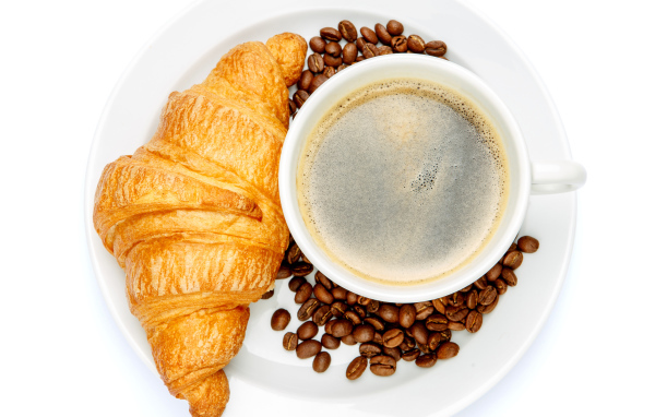 Чашка кофе на белой тарелке с круассаном и зернами, вид сверху 