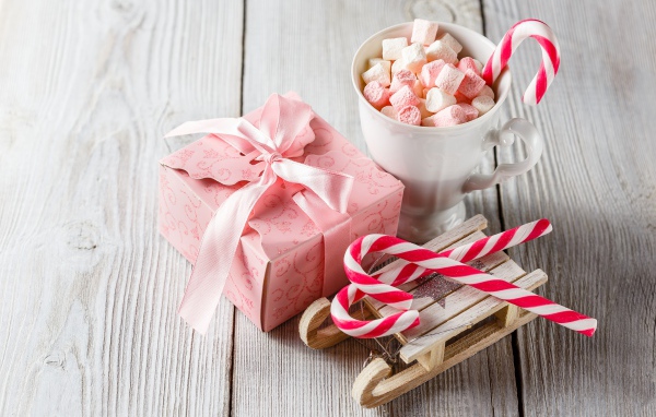 Чашка с маршмеллоу на столе с игрушечными санками и подарком