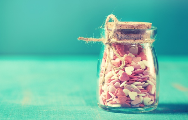 Стеклянная банка с маленькими конфетами в форме сердца на голубом фоне