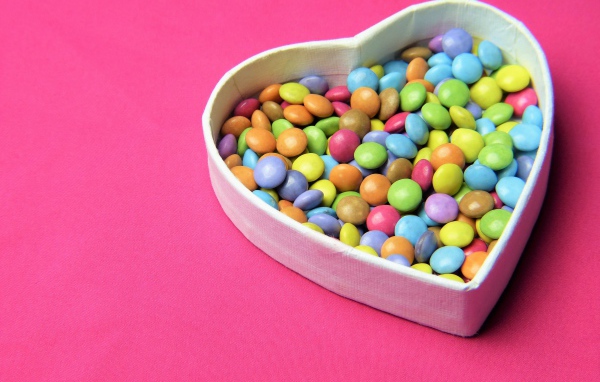 Heart shaped box with multicolored chocolates on pink background