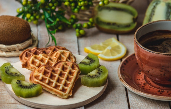 Вафли в форме сердца на доске с киви и чашкой кофе