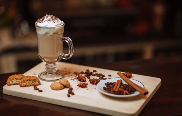 Горячее какао со сливками на столе с печеньем, зернами кофе и пряностями 