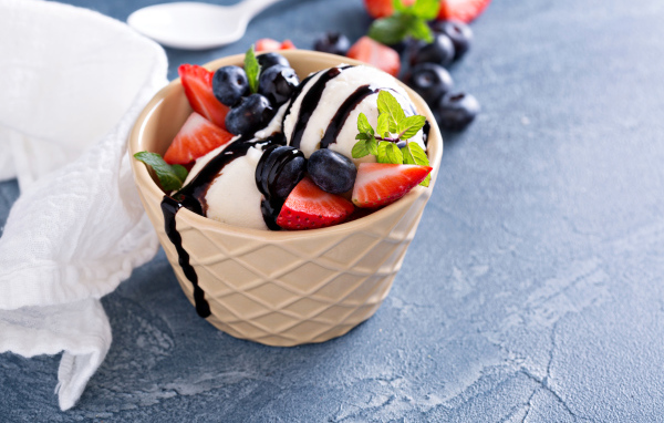 Шарики мороженого в стакане на столе с клубникой и ягодами черники