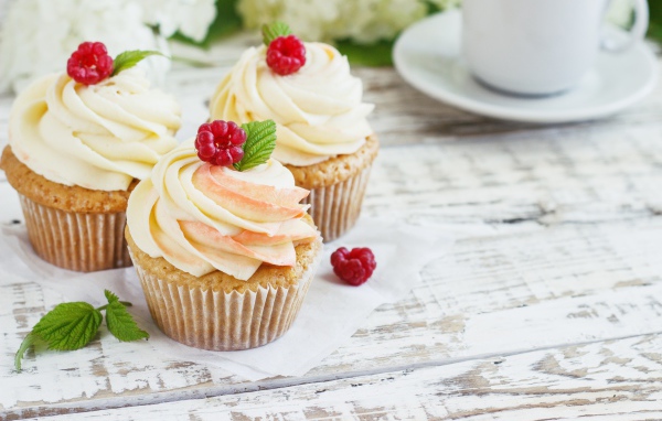 Три кекса с кремом на столе с чашкой кофе