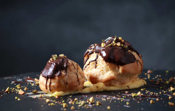 Два заварных пирожных с шоколадом на сером фоне