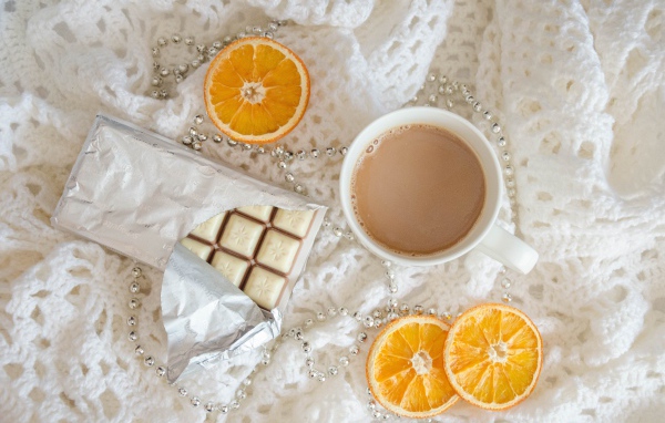 Чашка какао, шоколад и апельсин на белом пледе