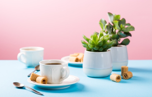 Чашка кофе на блюдце с вафлями на столе с цветами