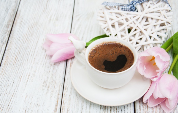 Чашка кофе на столе с розовыми тюльпанами и плетеным сердцем