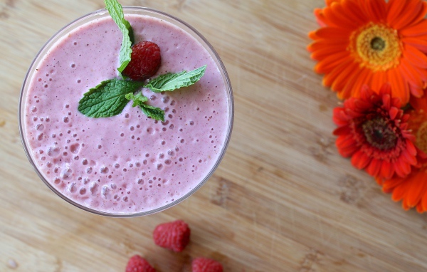 Малиновый смузи в стакане на столе с герберами