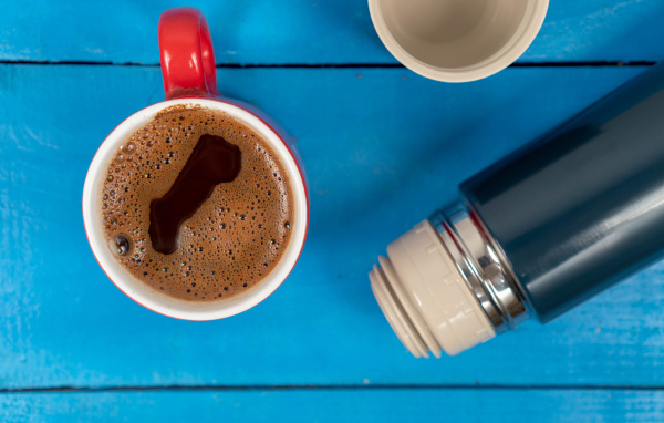 Красная чашка кофе с термосом на голубом столе 