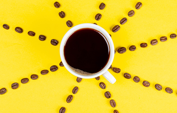 Солнце из чашки кофе с зернами на желтом фоне