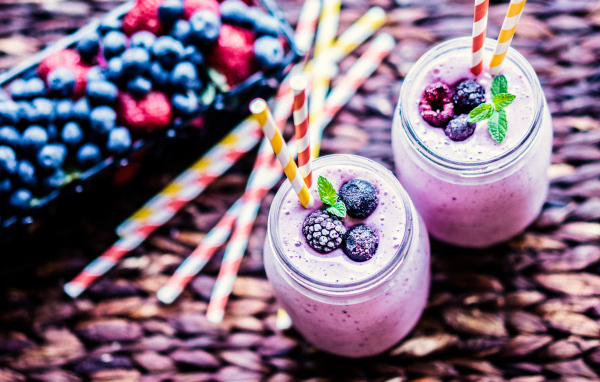 Две банки смузи с трубочками на столе с ягодами