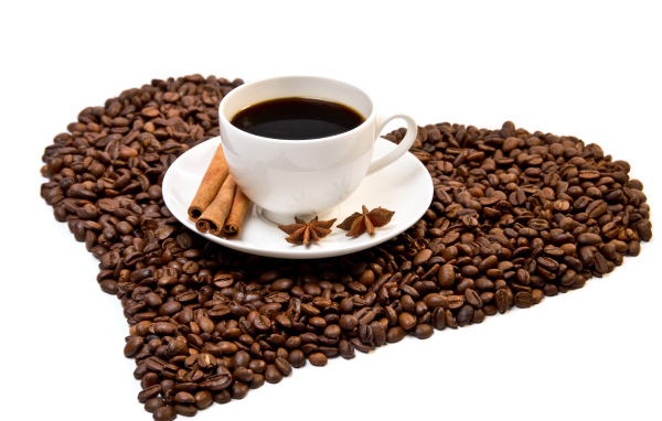 Белая чашка с корицей и бадьяном стоит на кофейных зернах на белом фоне