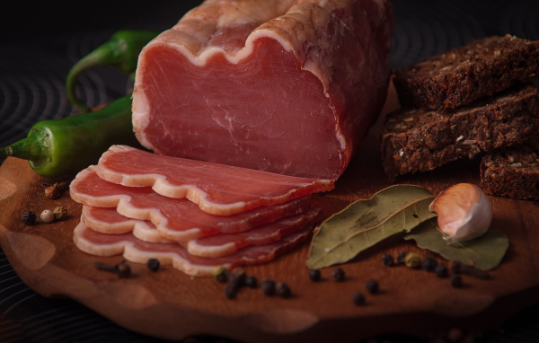 Кусок вяленого мяса на доске с черным хлебом и специями