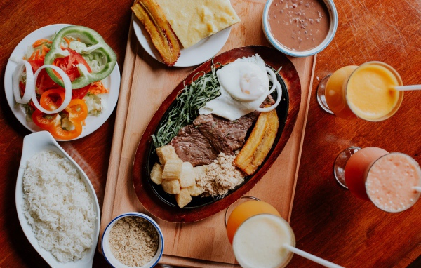 Кусок мяса в жаровне на столе с напитками, овощами и рисом