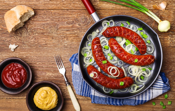 Колбаски барбекю с луком на сковороде на столе с соусом