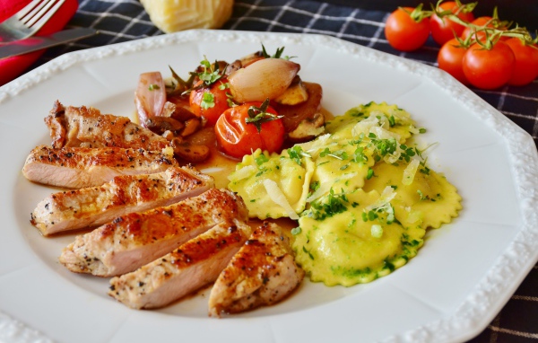 Куриное филе нарезанное кусочками на тарелке с овощами и варениками