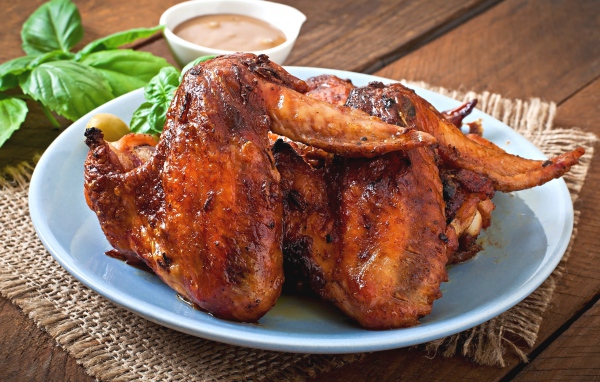 Зажареные куриные крылышки на столе с соусом и базиликом