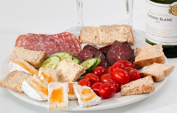 Тарелка с мясными продуктами, яйцами, овощами и хлебом на столе с вином