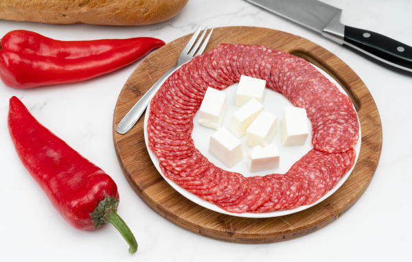 Тарелка с колбасой и сыром на столе с красным перцем