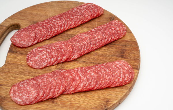 Колбаса тонко нарезана на разделочной доске 