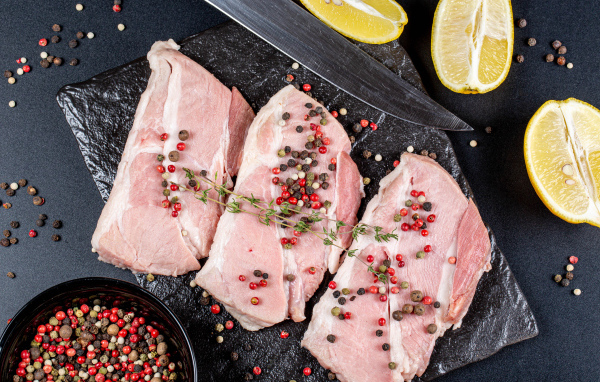 Куски свежего мяса на столе с зернами перца и лимоном