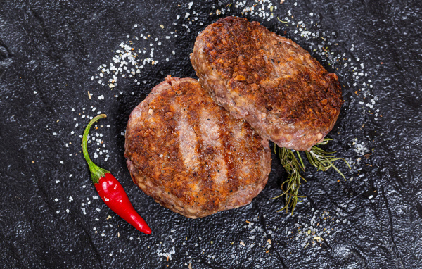 Две котлеты на черной поверхности с красным перцем