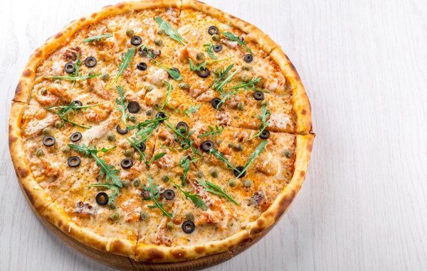 Пицца с морепродуктами, рукколой и оливками на столе 