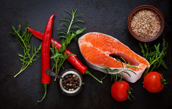 Кусок свежей красной рыбы на столе со специями, красным перцем и помидорами