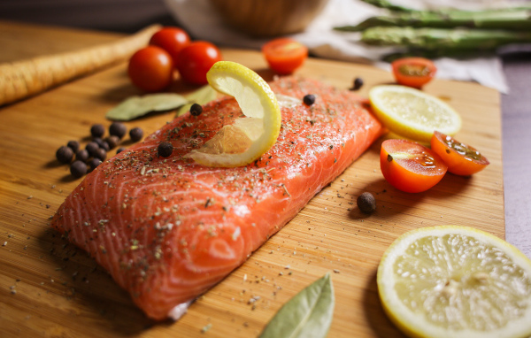 Кусок красной рыбы на доске с лимоном и помидорами