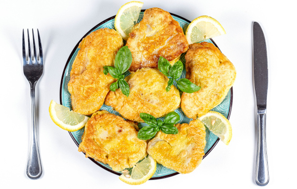 Аппетитная рыба в кляре на тарелке с кусочками лимона и столовыми приборами