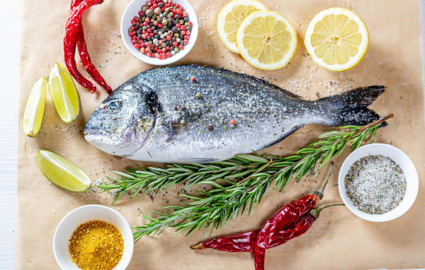 Свежая рыба на столе со специями, лимоном, розмарином и красным перцем