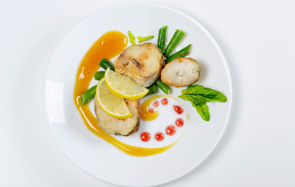 Кусочки жареной рыбы на белой тарелке с лимоном и зеленью
