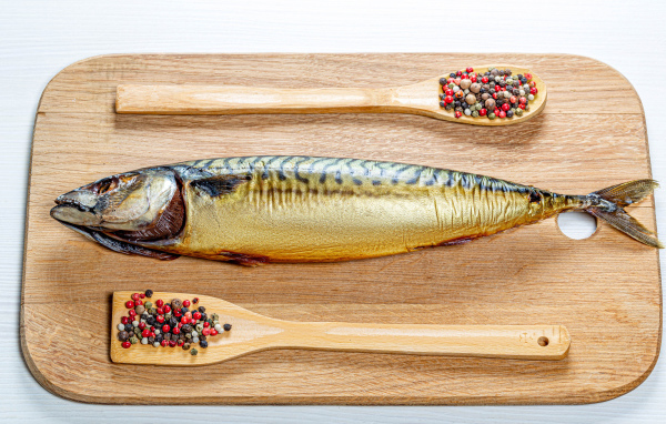 Копченая скумбрия на разделочной доске с перцем на белом фоне