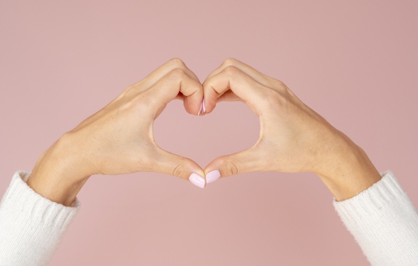 Девушка делает сердце руками на розовом фоне 