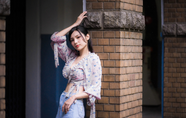 Красивая девушка азиатка стоит у кирпичной колонны 
