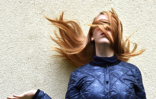 Девушка с волосами на лице стоит у стены