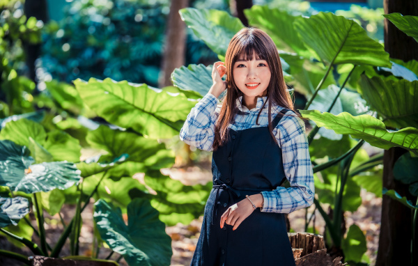 Улыбающаяся девушка азиатка в черном платье стоит в парке